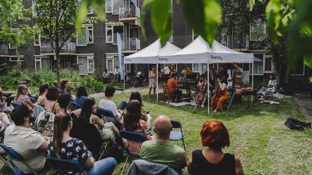 orchestra playing under a tent, in a garden of a building complex, public watching seated